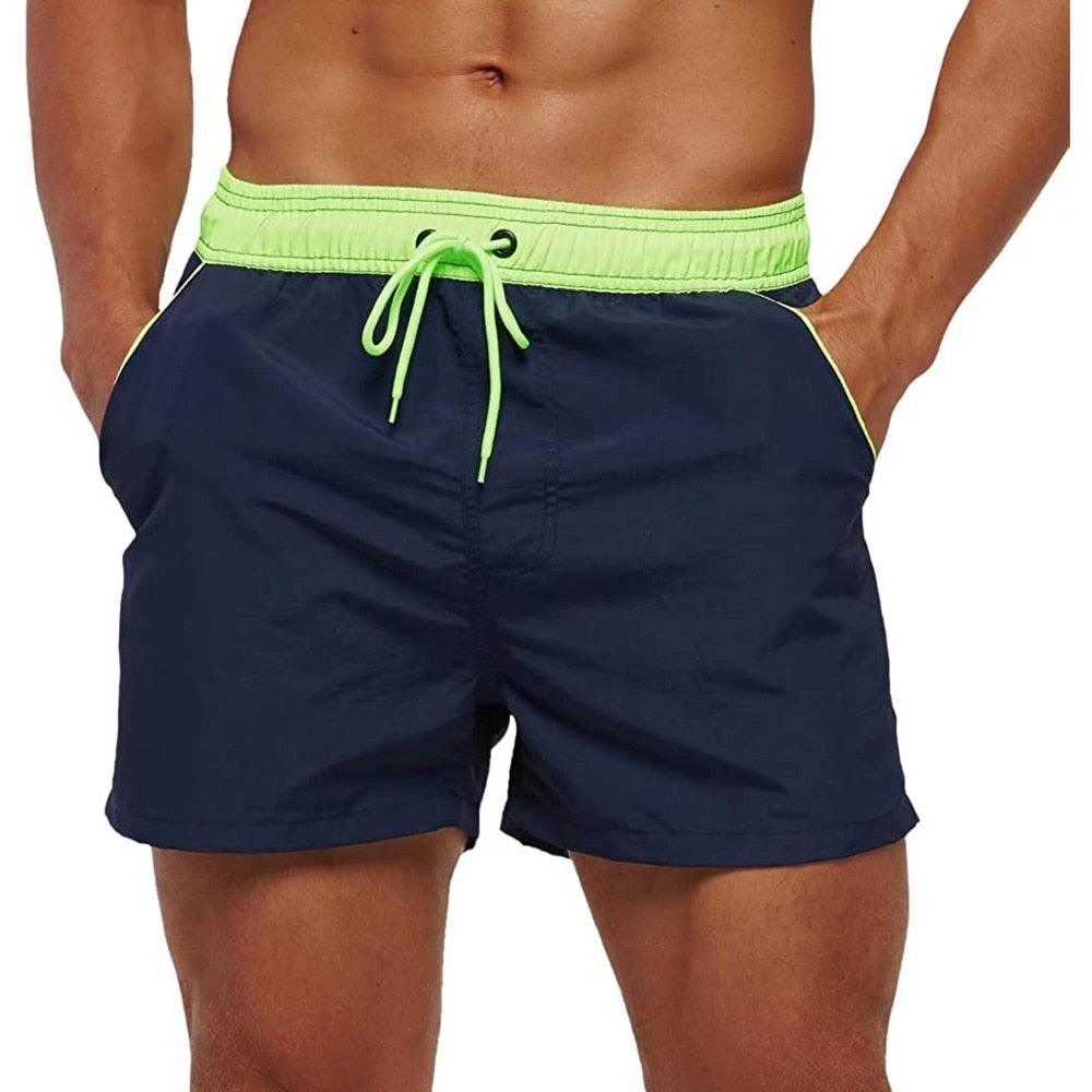 Men wearing sporty, regular fit navy swim trunks with a contrasting drawstring at the beach.