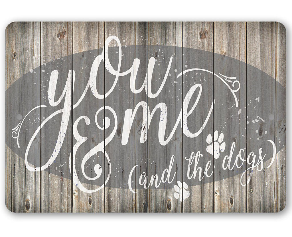 Rustic metal sign featuring the text You Me & The Dogs with paw prints on a wood plank background