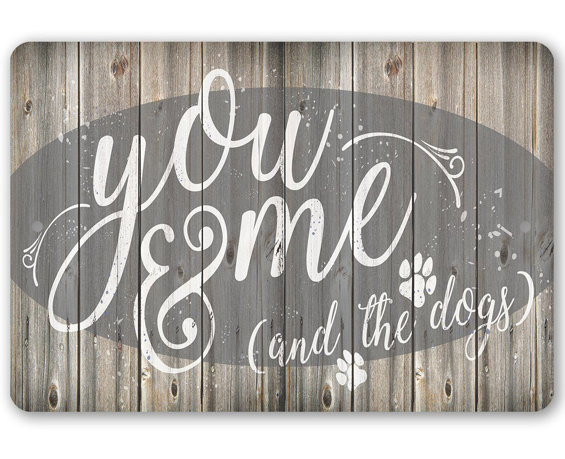 Rustic metal sign featuring the text You Me & The Dogs with paw prints on a wood plank background