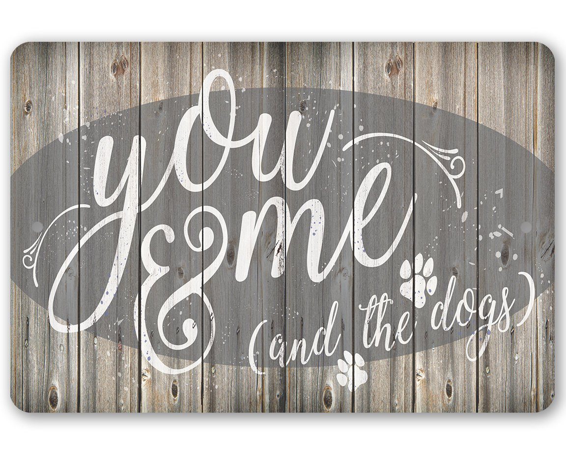 Rustic metal sign featuring the text You Me & The Dogs with paw prints on a wood plank background