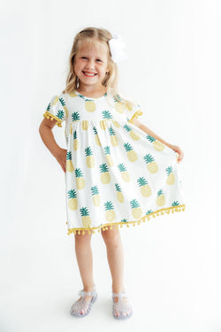 Girl wearing a Pineapple Pom Pom dress with colorful pom-pom trim on sleeves and hem.