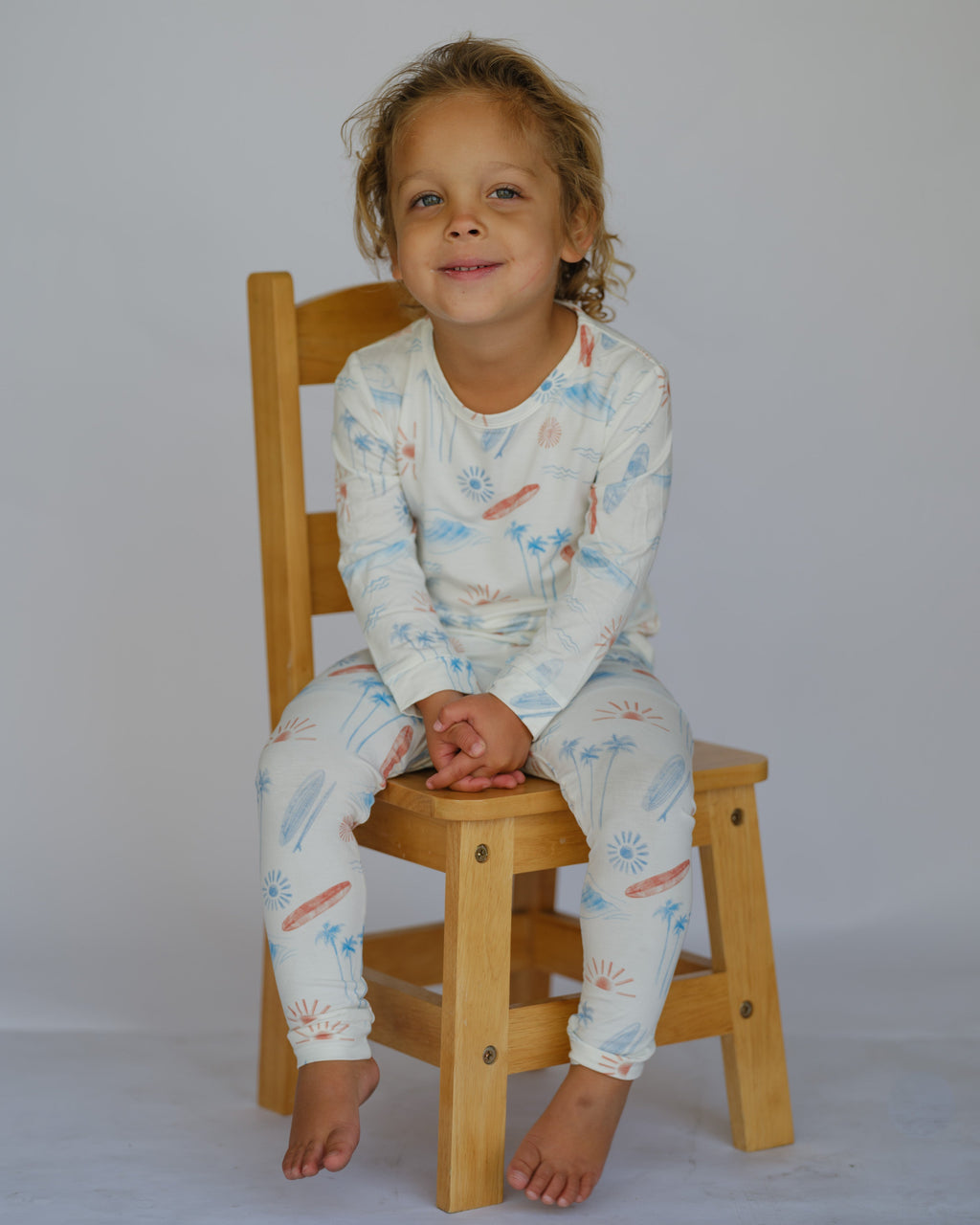 Child wearing a patterned outfit sitting on a wooden chair against a plain background