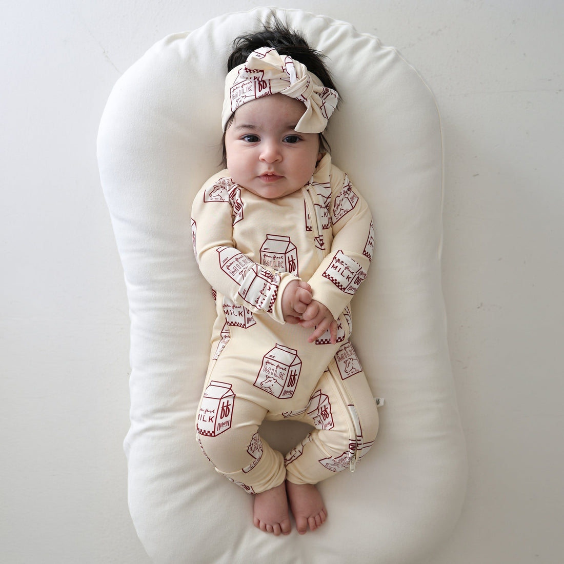 Baby wearing a one-piece bamboo zip pajama with a brown milk carton print pattern