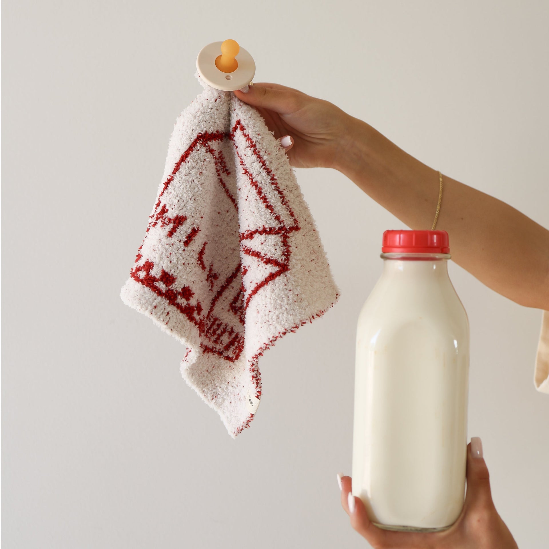 Plush baby lovey in a milk carton print held by a hand next to a glass bottle