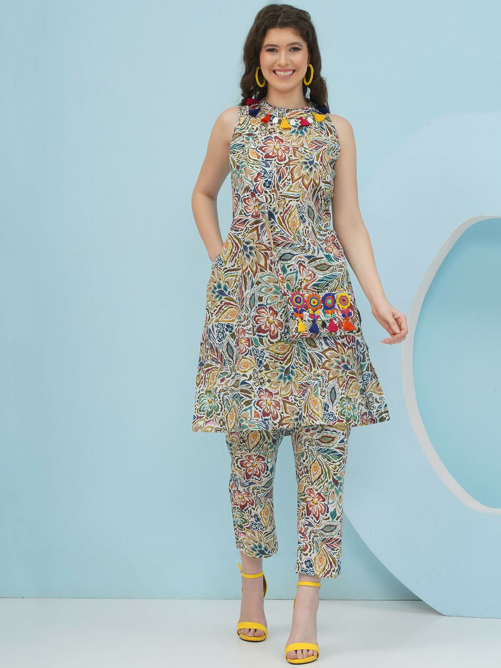 Woman wearing a multi-color floral co-ord set with an embellished sling bag, featuring mustard, rust, and teal tones on off-white cotton.