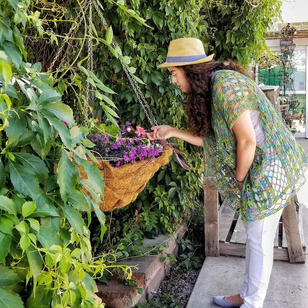 A woman wearing a bohemian, oversized, variegated green, blue, and yellow open knit crochet poncho outdoors.