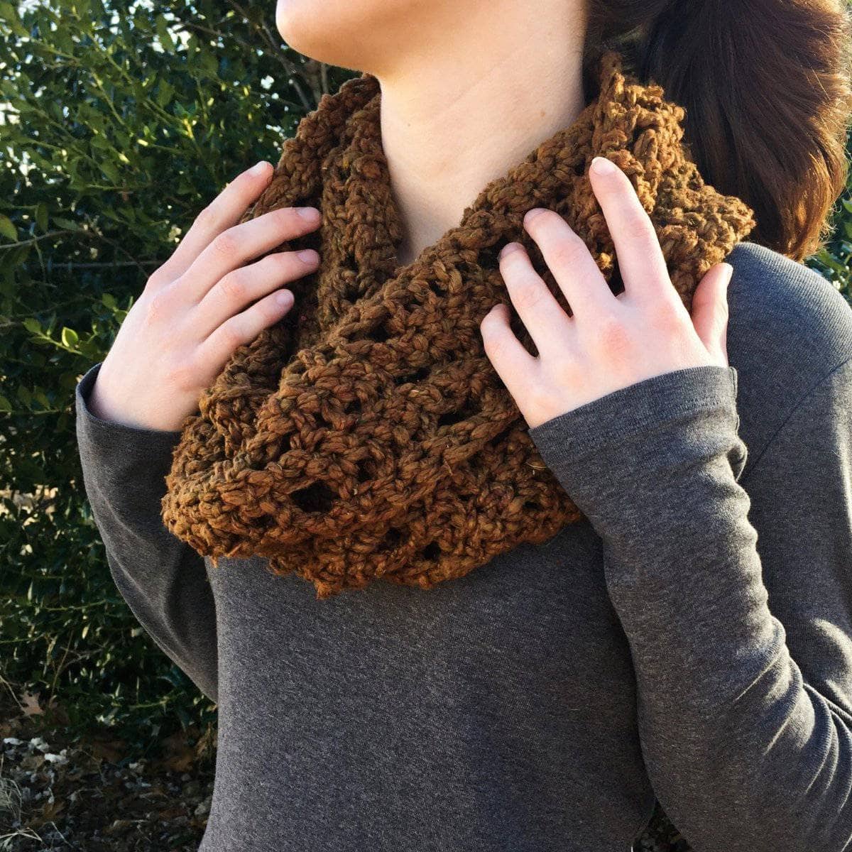 Woman wearing a chunky brown and bronze crocheted mobius cowl in a cozy bohemian setting.