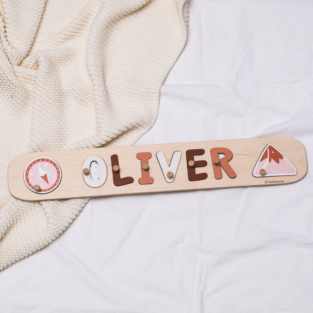 Minimalist wooden mountain name puzzle in neutral, terracotta, and pink tones displayed on a nursery wall.