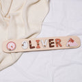 Minimalist wooden mountain name puzzle in neutral, terracotta, and pink tones displayed on a nursery wall.