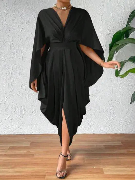A woman wearing a black pleated wave dress with cape sleeves and a front slit