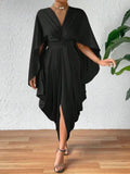 A woman wearing a black pleated wave dress with cape sleeves and a front slit