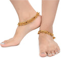 A pair of gold-polished white metal traditional Indian anklets on a neutral background