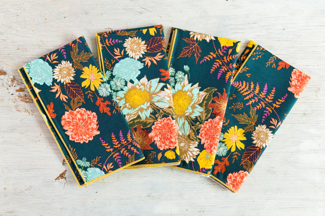 A set of four Winter Blue floral cloth napkins with a vibrant botanical print, featuring yellow, coral, and teal flowers on a deep blue background.