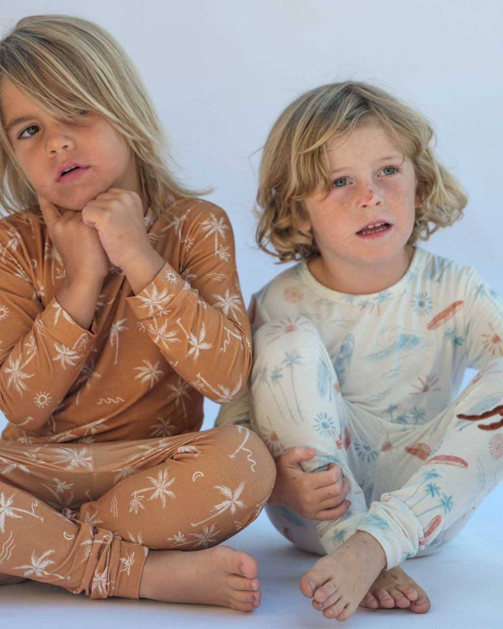Two children wearing patterned pajamas sitting on a white background