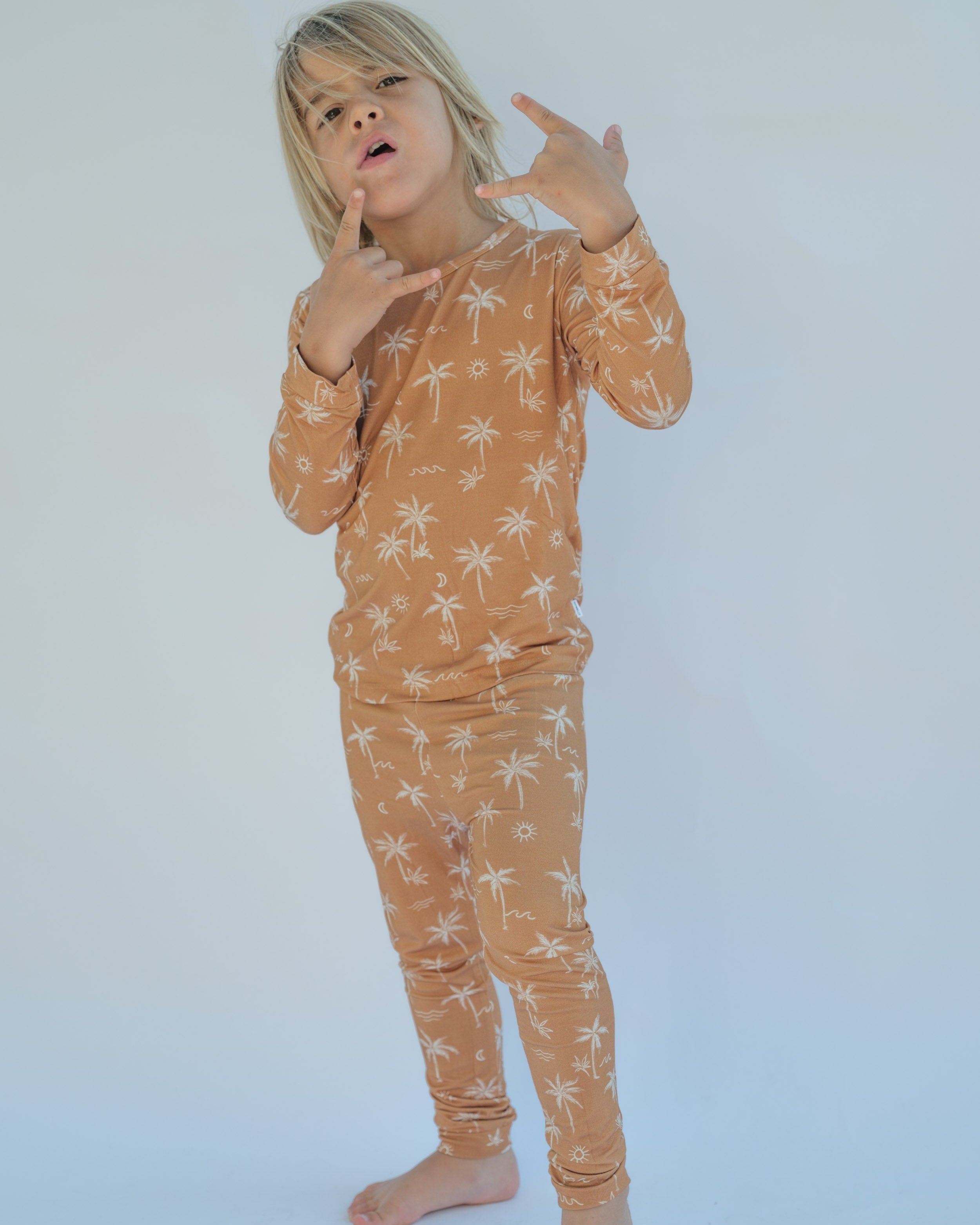 Child wearing a long-sleeve top and pants with palm tree pattern on a white background