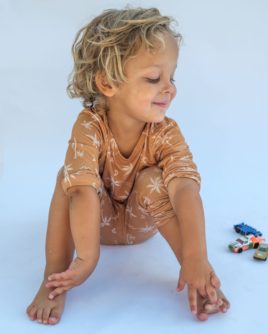 Child wearing a brown onesie with white patterns, sitting on a light blue background with toys.