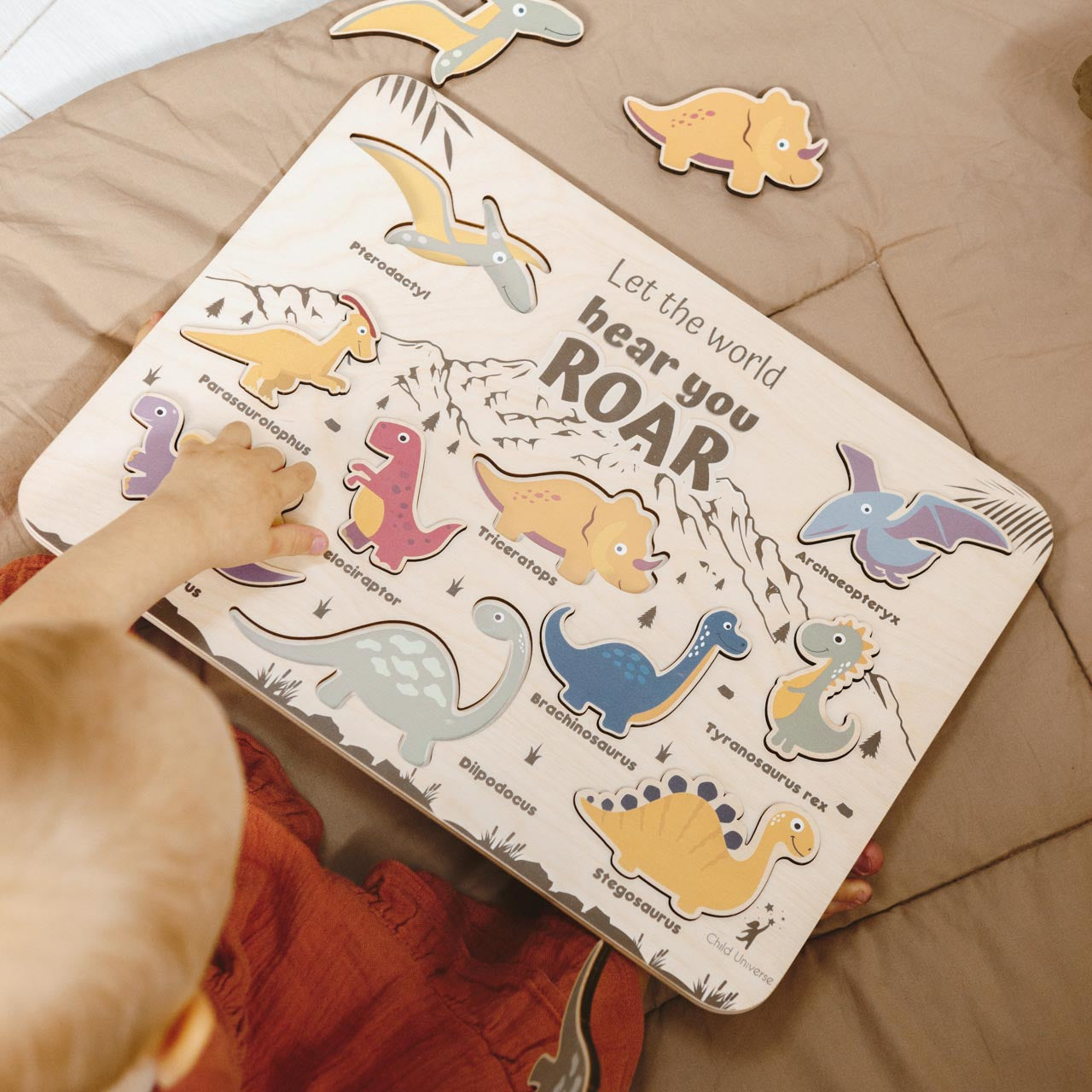 Minimalist wooden dinosaur puzzle with colorful prehistoric creatures on a neutral wooden board in a modern nursery setting.