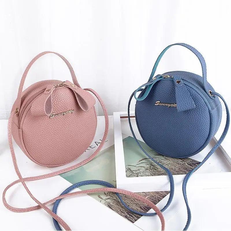 A stylish circular leather crossbody bag in solid pink, featuring a zip closure and minimalist design.