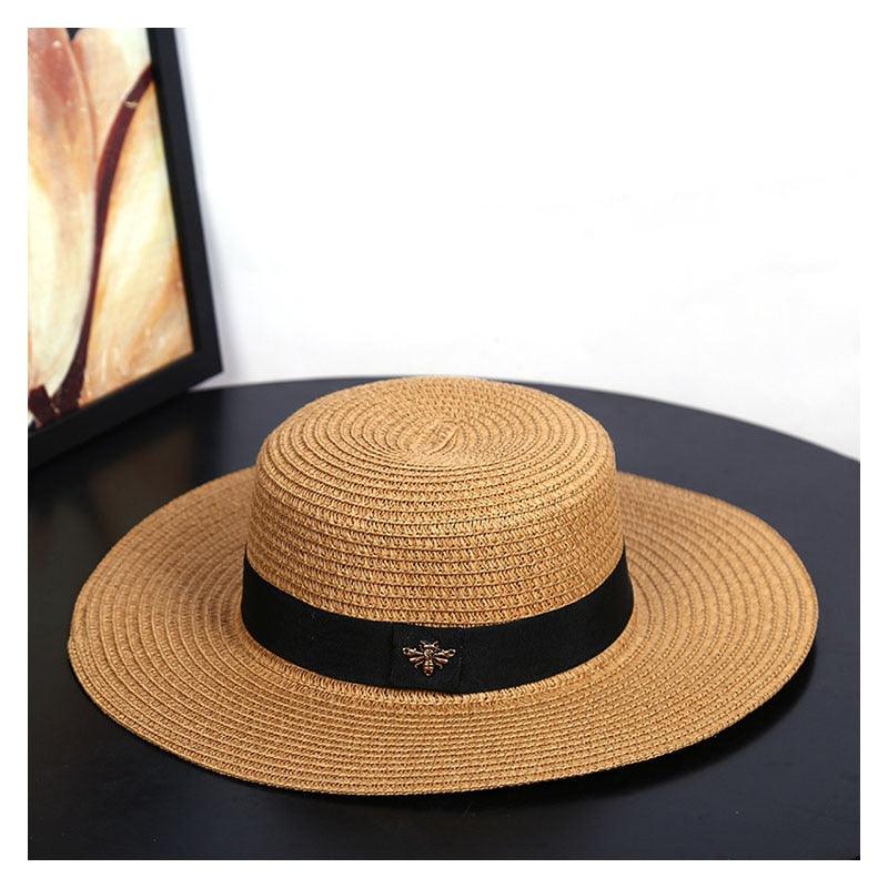 Women's tan straw sun hat with a wide brim and a black decorative band with a metallic accent.