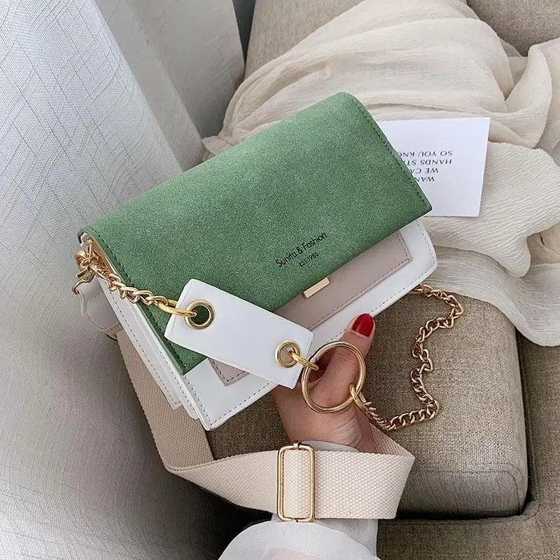 A modern, contrast-color scrub leather crossbody bag featuring a delicate chain shoulder strap.