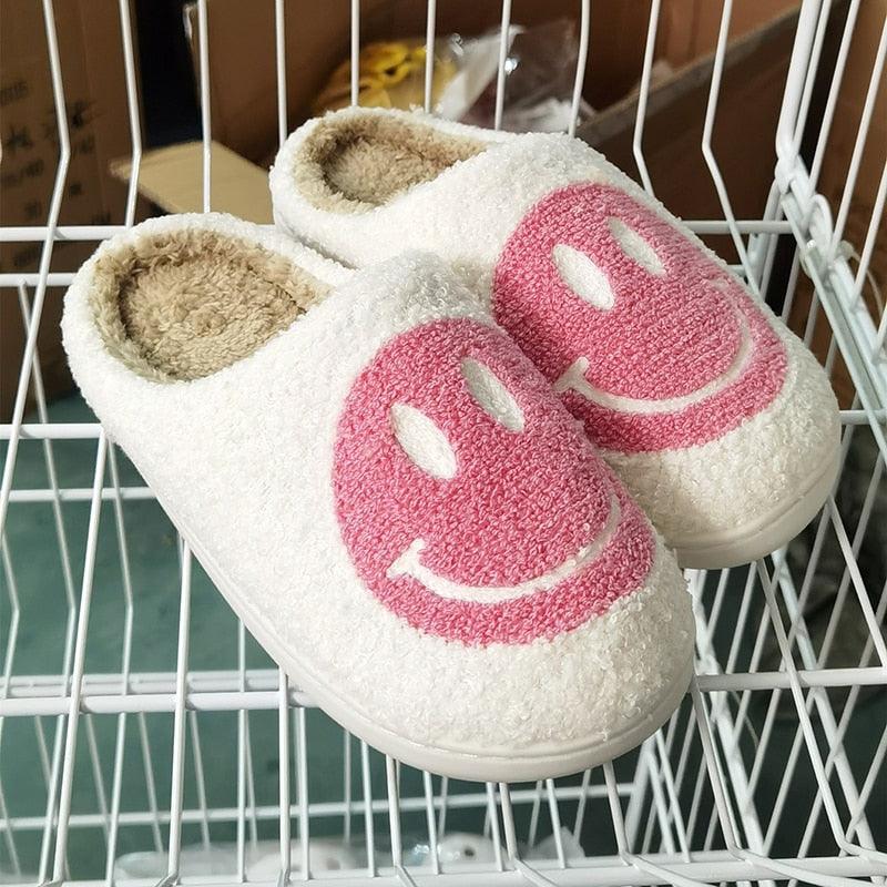 Pink plush smiley face slippers with anti-slip soles for indoor house use.