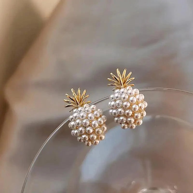 Close-up of gold pineapple-shaped stud earrings with a round white pearl on a person's ear.