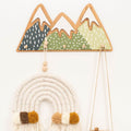 Set of gender-neutral mountain-themed wall hooks mounted on a nursery wall for kids' clothing organization.