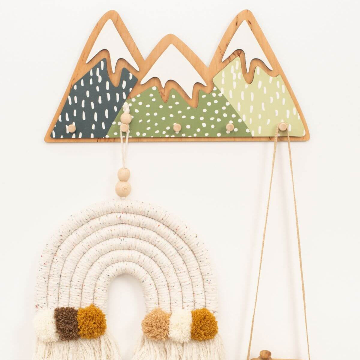 Set of gender-neutral mountain-themed wall hooks mounted on a nursery wall for kids' clothing organization.