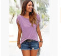 A woman wearing a beige short sleeve t-shirt with fringe tassel details on the sleeves, paired with denim shorts.