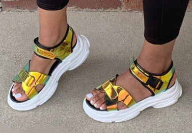 Close up of a pair of women's metallic blue and gold platform sandals with thick white soles on a sidewalk.