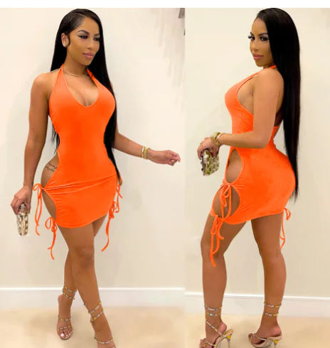 A woman wearing a vibrant orange backless halter mini dress with adjustable side drawstring ties, captured in a studio setting.