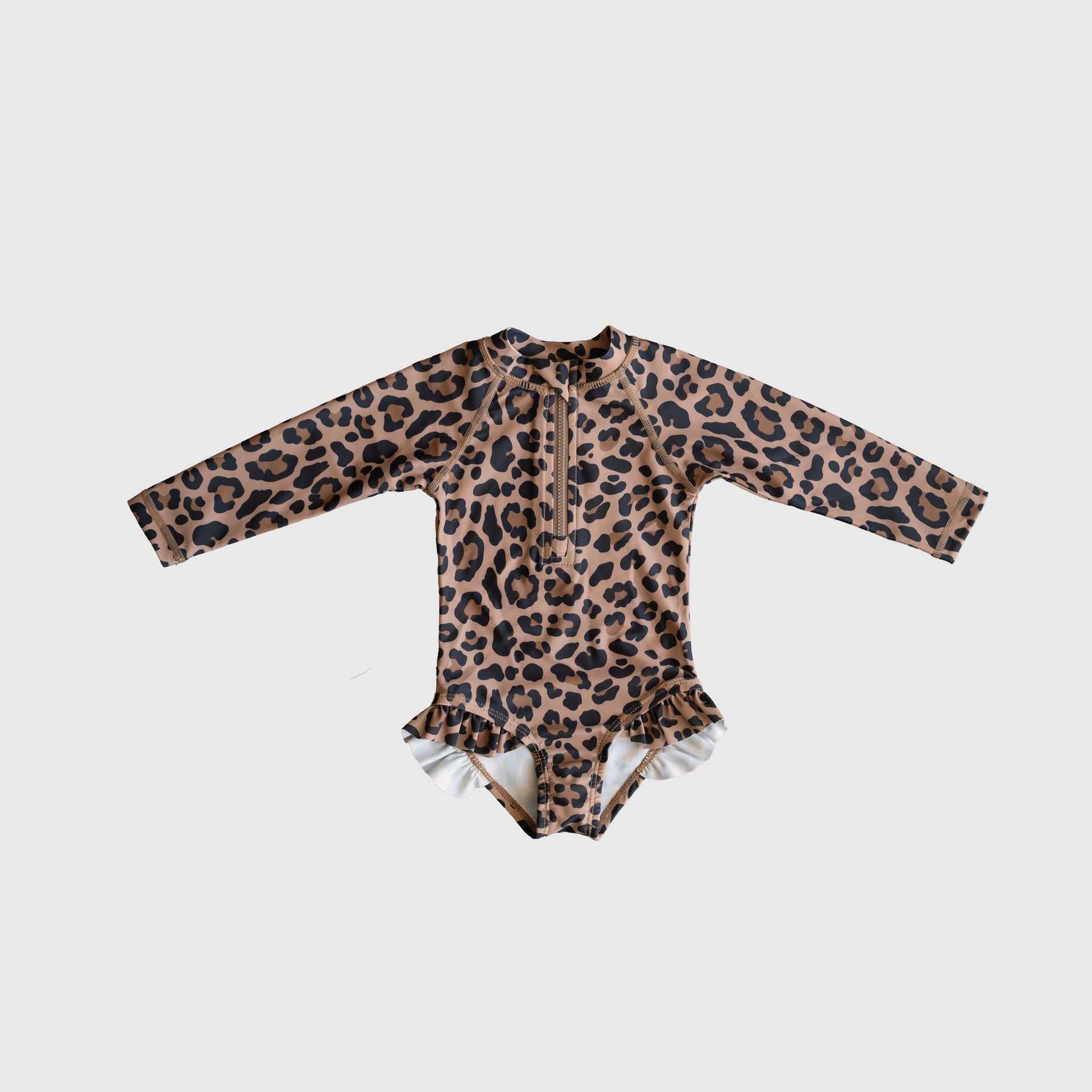 Girl wearing a long sleeve leopard print one-piece swimsuit with ruffle leg details and a front zipper at the beach.