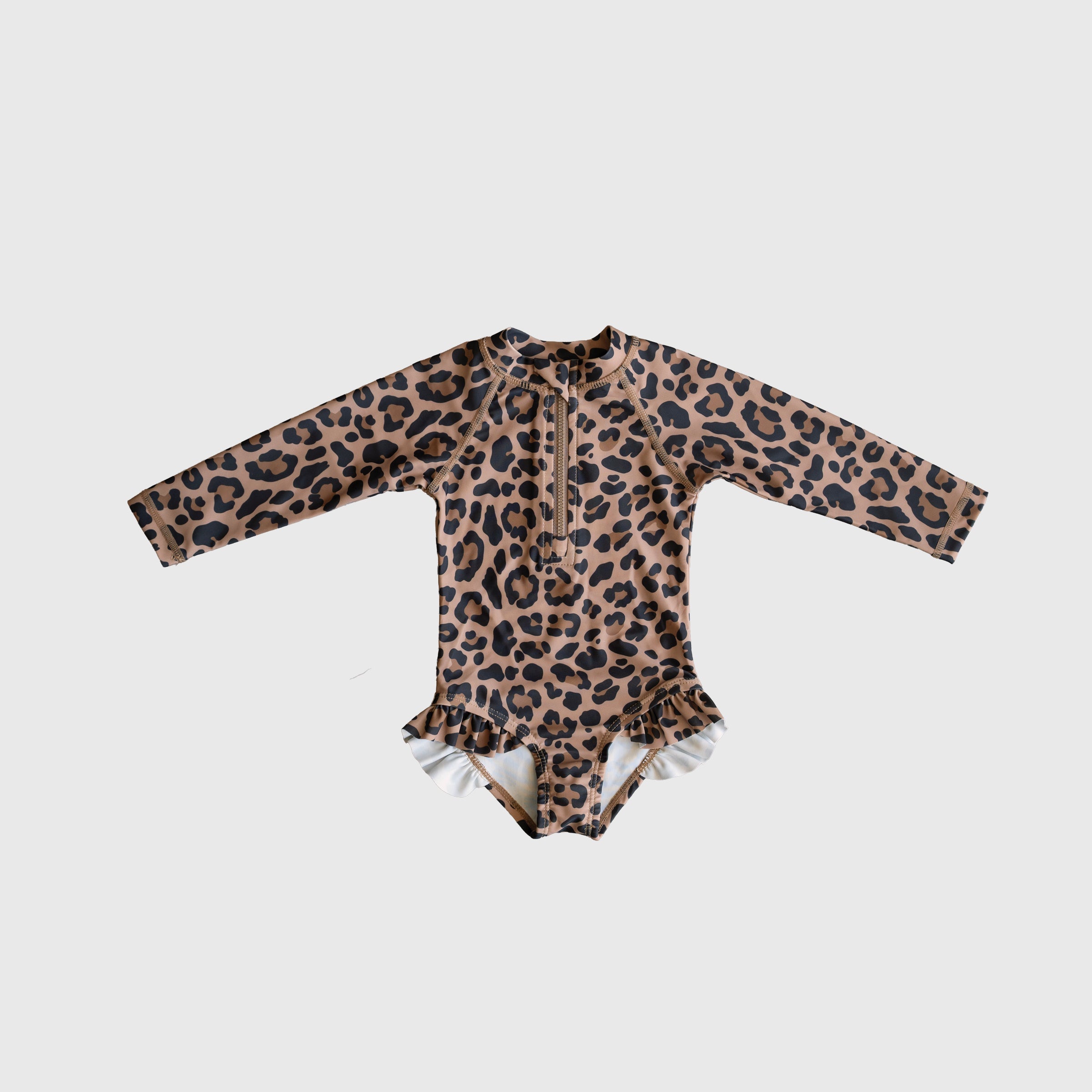 Girl wearing a long sleeve leopard print one-piece swimsuit with ruffle leg details and a front zipper at the beach.