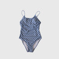 Woman wearing a classic polka dot one-piece swimsuit in navy blue with adjustable shoulder straps.