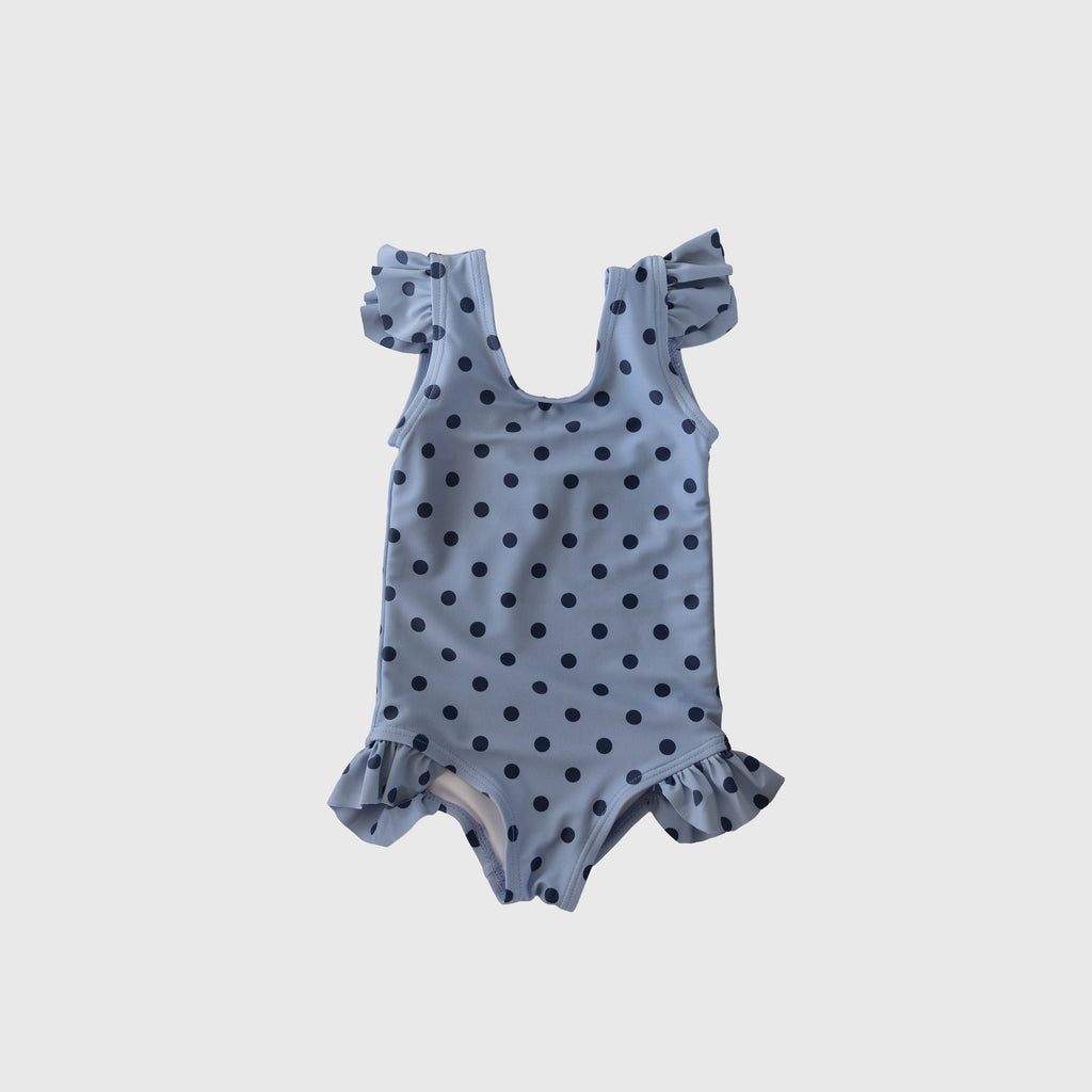 Girl wearing a light blue and navy polka dot one-piece swimsuit with ruffle shoulder and leg details