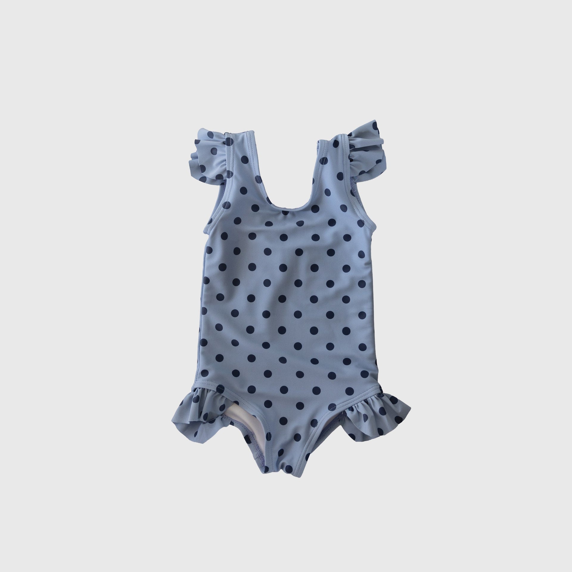 Girl wearing a light blue and navy polka dot one-piece swimsuit with ruffle shoulder and leg details