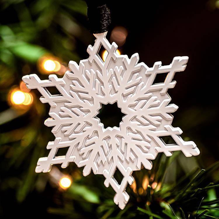 White metal snowflake ornament hanging on a Christmas tree with golden lights in the background