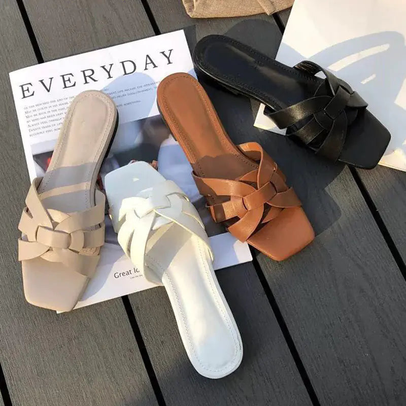 Top view of three pairs of braided synthetic leather flat slide sandals in beige, white, and brown on a wooden background