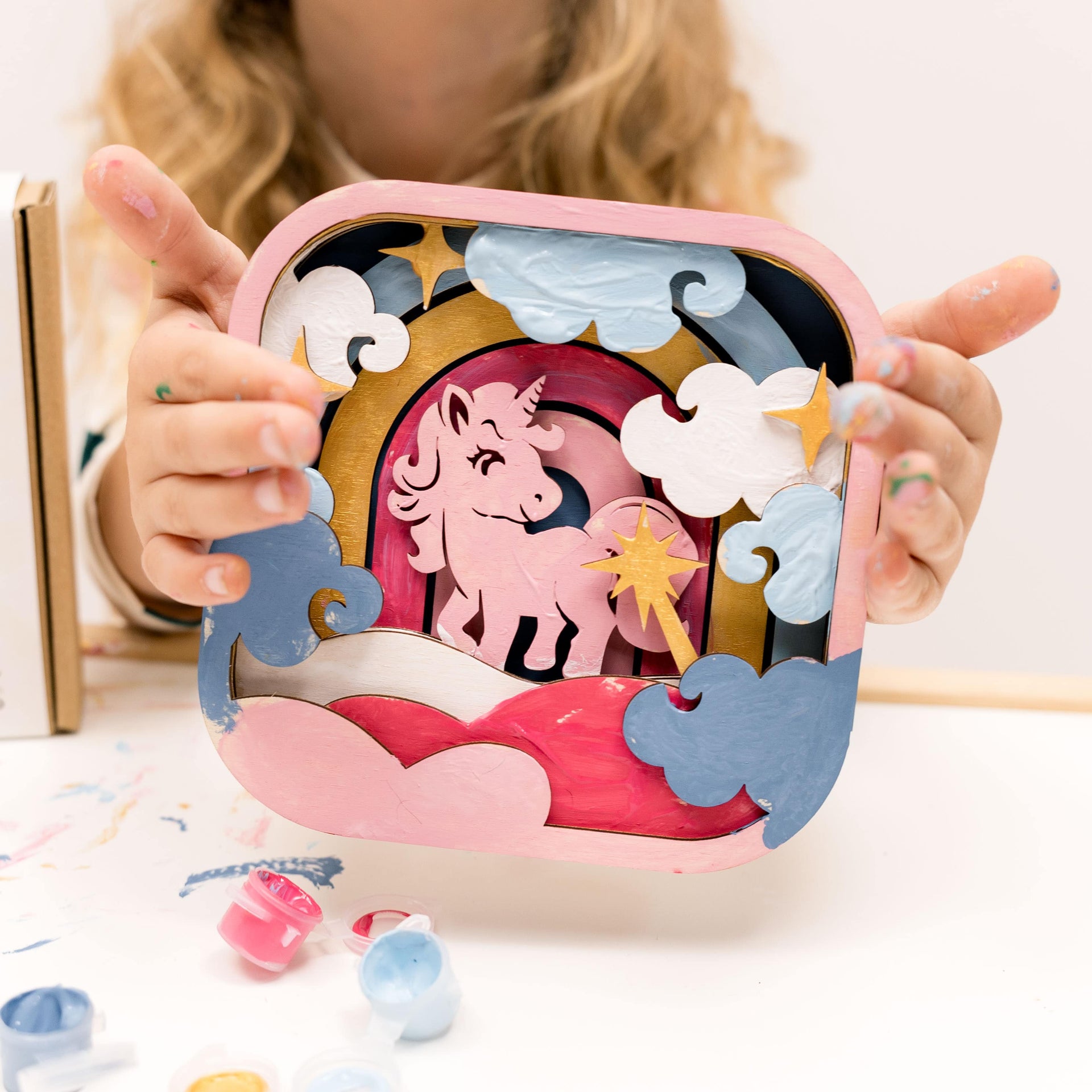 3D DIY wooden unicorn craft kit with primary color paints and a paint brush on a neutral background.