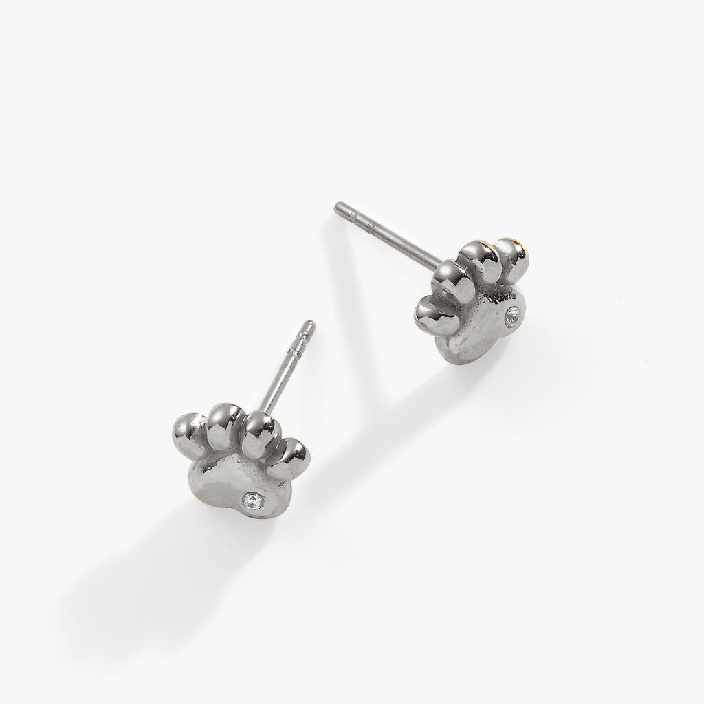 A pair of minimalist polished silver paw print stud earrings with small crystal accents.