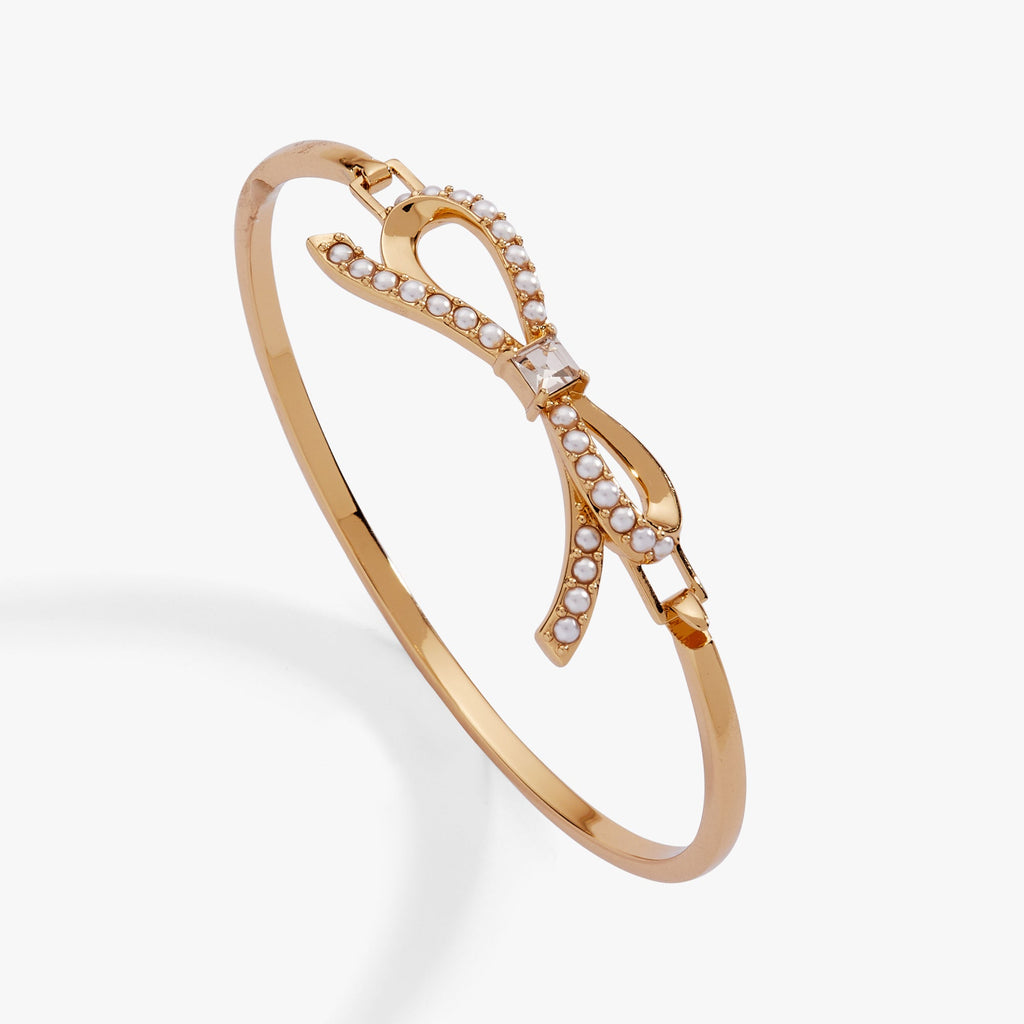 Gold-plated tension bangle featuring a pearl rosary chain, dimensional bow, and clear crystal accent.