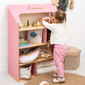 Pink and white Montessori-inspired dollhouse bookcase featuring open shelving in a child's bedroom.