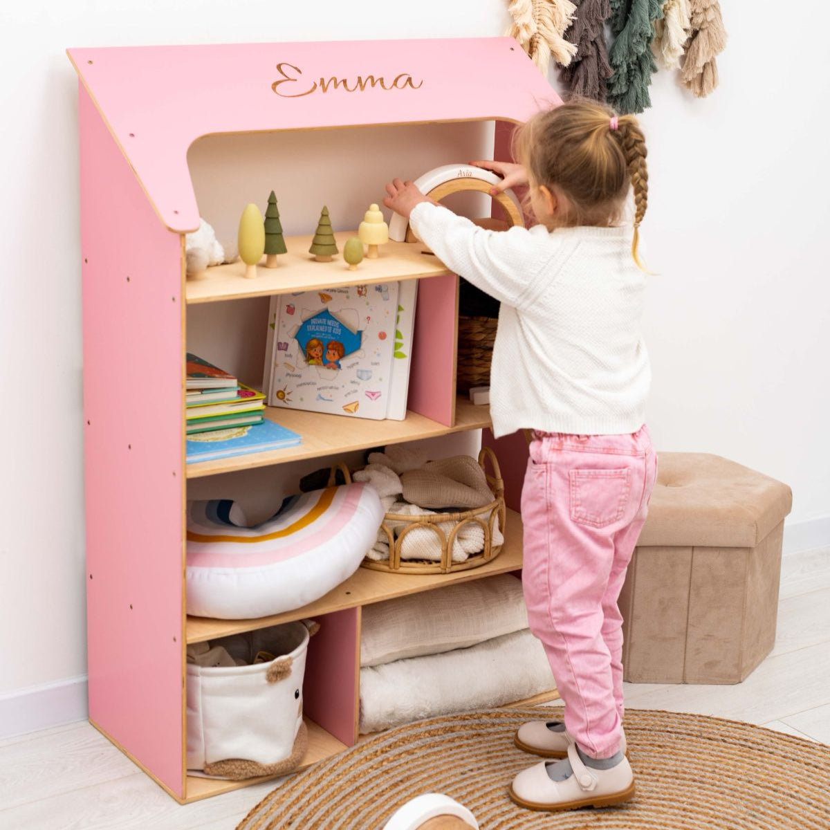 Pink and white Montessori-inspired dollhouse bookcase featuring open shelving in a child's bedroom.