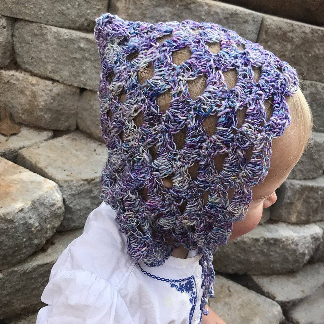 Vintage-inspired pixie bonnet in variegated pastel purple, blue, and white yarn worn by a child.