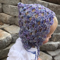 Vintage-inspired pixie bonnet in variegated pastel purple, blue, and white yarn worn by a child.