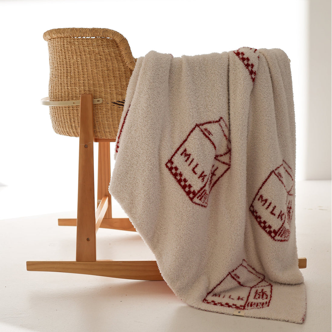 Plush milk carton print blanket in cream and red draped over a wicker baby bassinet