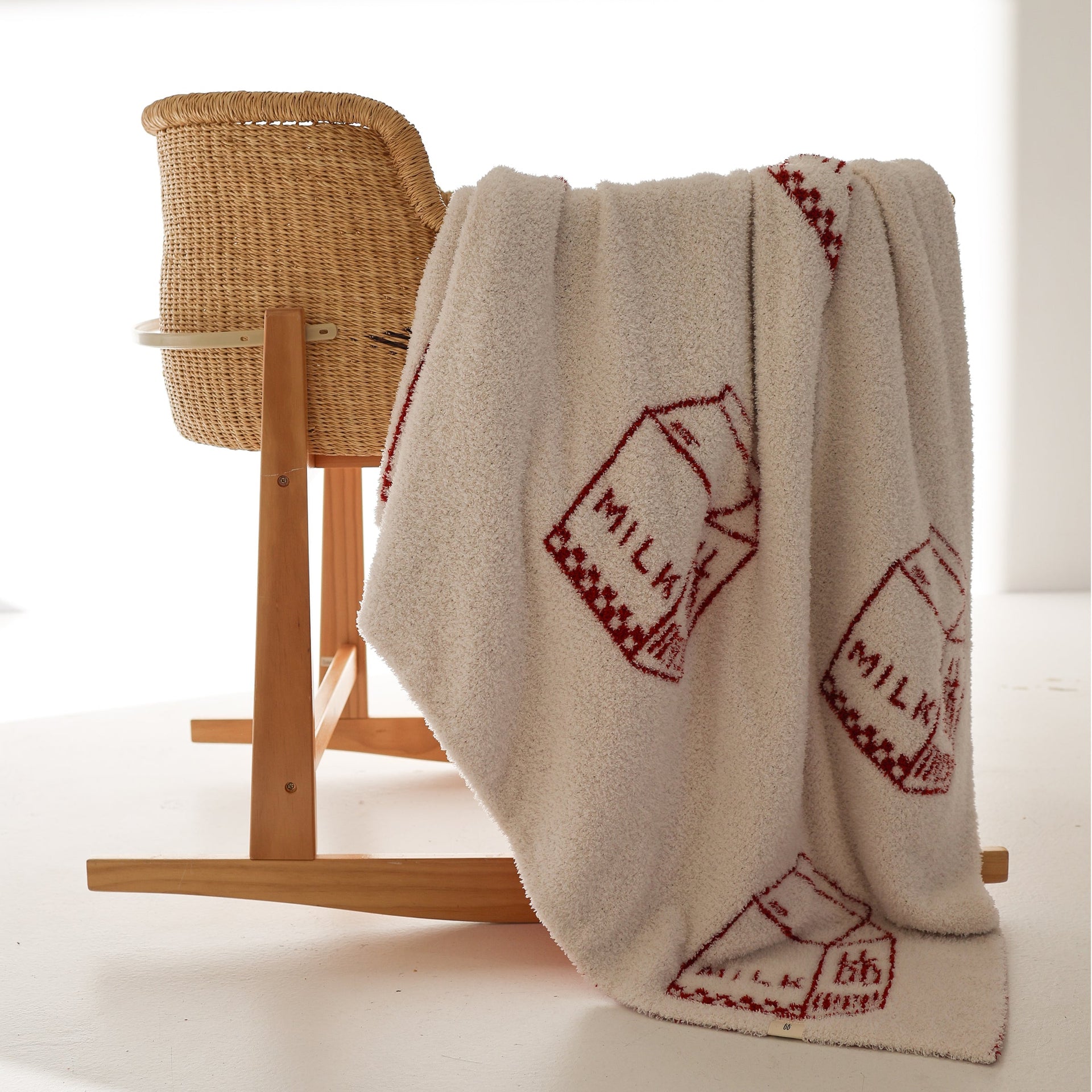 Plush milk carton print blanket in cream and red draped over a wicker baby bassinet