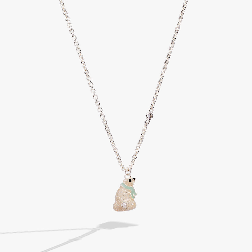 Close up of a whimsical polar bear pendant necklace with enamel, a jet stone eye, and crystal accents on a gold-tone chain.