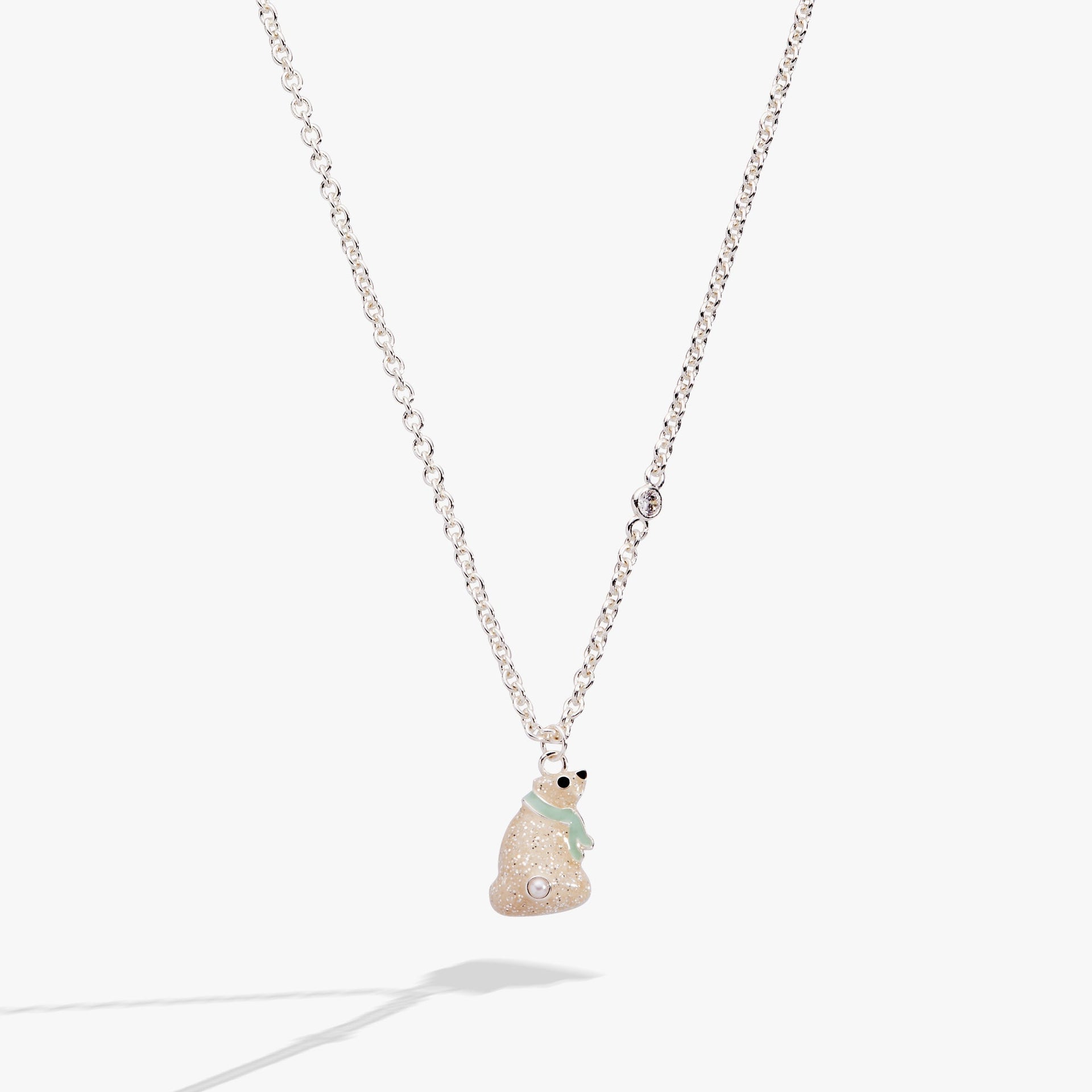 Close up of a whimsical polar bear pendant necklace with enamel, a jet stone eye, and crystal accents on a gold-tone chain.