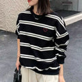 Woman wearing a black and white horizontal striped pullover sweater with a small red heart embroidery on the chest